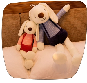 Close-up of plush rabbit dolls in blue and red overalls sitting on a cozy bed