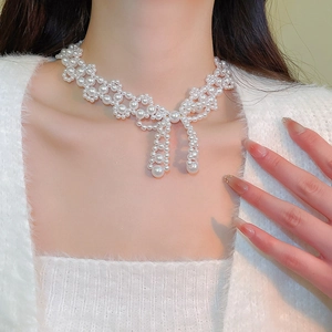 Detail shot of a white pearl bow necklace worn elegantly on a neck with a soft background