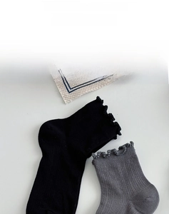 Close-up of ribbed knit cotton socks featuring delicate lace ruffled cuffs in black and grey