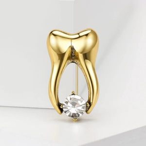 Golden tooth-shaped alloy brooch with clear round crystal on white geometric background
