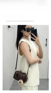 Mirror selfie showing a brown leather Boston bag with plush charm and black sunglasses