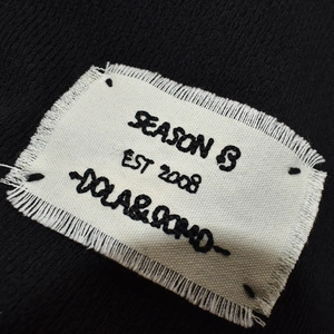 Dettaglio del tessuto in maglia nera e dell'etichetta bianca ricamata Season 8