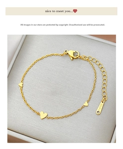 Close-up of golden stainless steel heart charm bracelet with lobster clasp on a grey jewelry box