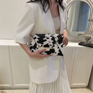 Modern cow print envelope clutch bag with gold trim detail held by a stylish woman