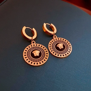 Detailed macro view of rose gold Medusa pendant earrings with Greek key engraved patterns
