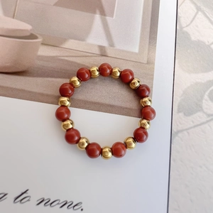 Elastic red stone bead ring with gold accents displayed on a minimalist magazine