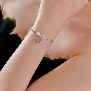 Close-up of beaded silver bracelet with white pearl and pink heart pendant on model