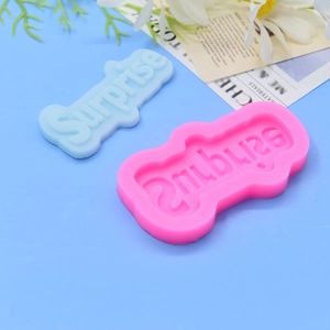 Moule en silicone rose avec lettre 'Surprise' et produit bleu sur fond floral bleu