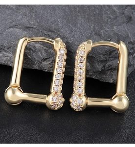 Macro shot of geometric gold hoop earrings with white zircon on dark stone background