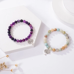 Detailed close-up of pink zebra stone bracelets with tree of life charms on white blocks