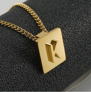 Close-up of gold square necklace pendant with embossed letter K on fine link chain