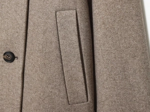 Détail macro d'un manteau en laine camel montrant le tissu, la poche et le bouton noir