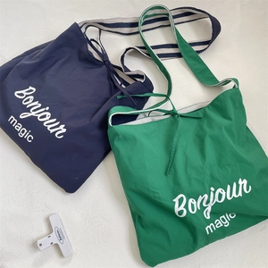 Detail of navy and green canvas tote bags with striped straps and Bonjour magic print