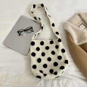Close-up of fluffy white plush crossbody bag with black polka dots on textured fabric