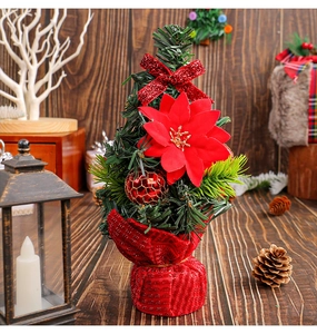 Mini Christmas tree with red poinsettia flowers and plaid base on a wooden desk