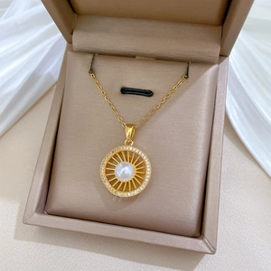 Close-up of a gold hollow pendant with central white pearl and diamond halo in a jewelry box