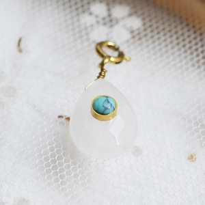 Macro detail of teardrop gemstone pendant with gold wire wrap on white lace fabric