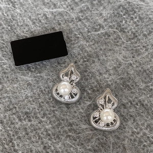 Macro shot of silver hollow gourd earrings featuring white pearl and sparkling rhinestones