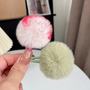 Detail of soft pink and light green faux fur pom pom hair clips held in hand