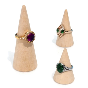 Three elegant rings displayed on wooden cone stands with colorful gemstones on white background