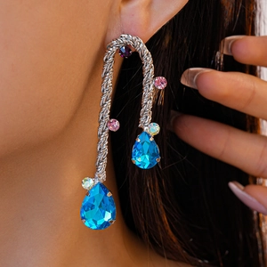 Close-up of woven silver tassel earring with blue teardrop crystals worn by a model