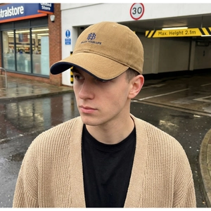 Detail of khaki cotton baseball cap with blue HB embroidery worn in a casual street setting
