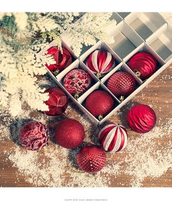 Detailed set of assorted red Christmas ornaments in a white gift box on snowy wood background