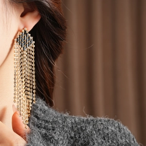 Close-up of gold fringe earrings with black rhinestones on a model wearing a grey sweater