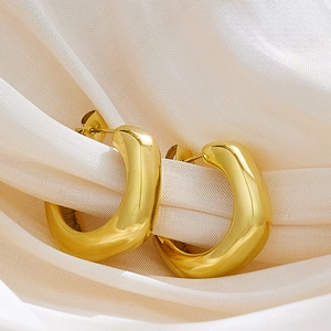 Macro shot of thick gold C-shape hoop earrings on elegant silk fabric background