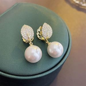 Close-up of gold leaf-shaped earrings with micro-set zircons and a white round pearl