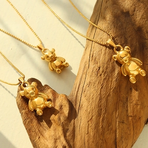Three 18K gold plated bear pendant necklaces hanging on a textured wooden branch