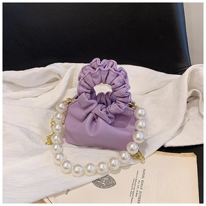 Detailed shot of purple pleated cloud handbag with white pearl strap on soft fabric