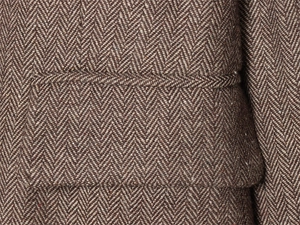 Close-up of herringbone wool fabric texture and pocket stitching detail on a blazer