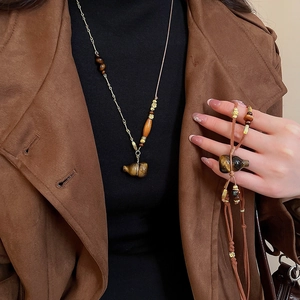 Detailed close-up of tiger eye stone gourd pendant necklace on a brown suede coat