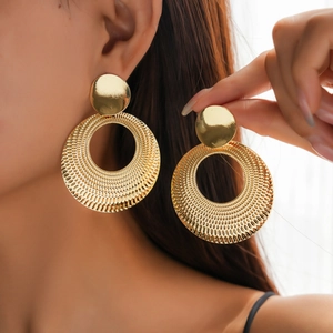 Close-up of golden hollow circular metal earrings with textured finish on model