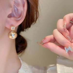 Close-up of elegant gold pearl earrings with geometric diamond square studs on model