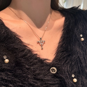 Detail of S925 silver cross and heart necklace worn by a model on a black background
