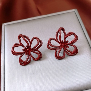 Close-up of wine red enamel flower earrings on a textured jewelry box with silk fabric