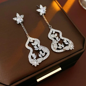 Detail shot of silver flower gourd earrings with clear crystals on a brown jewelry box