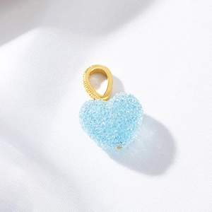 Sparkling light blue heart pendant with gold bail on a white textured background