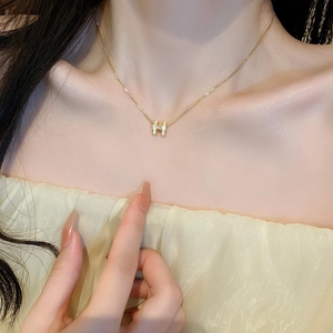 Close-up of gold-plated H-letter necklace with white enamel inlay on a model neck