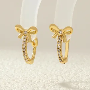Close-up of gold bow earrings featuring sparkling zircon inlay on a display stand