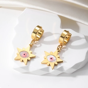Close-up of golden star drop earrings with pink evil eye on white silk fabric background