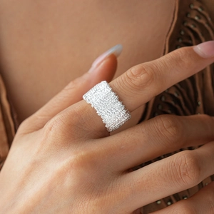 Detail of silver textured wide band ring with irregular lava surface worn on hand