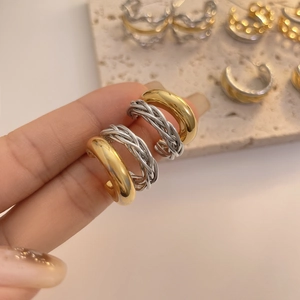 Detail von gedrehten und glatten C-förmigen Ohrringen in Gold und Silber auf einem Steintablett