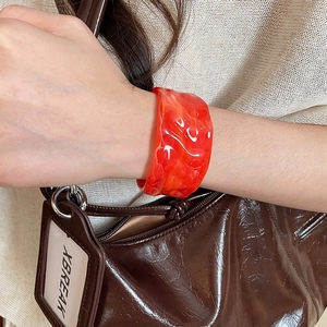 Detailed view of a wide red acrylic cuff bracelet with white marble texture on a wrist