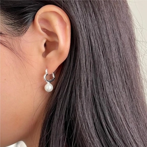 Close-up of heart shaped silver hoop earring with white pearl pendant worn by model