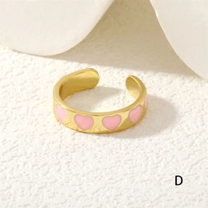 Detailed close-up of adjustable gold ring with pink enamel heart patterns on stone background