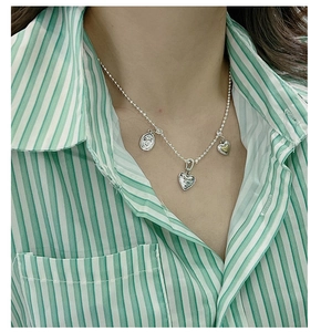 Detail of silver S925 heart and smiley face pendants on bead chain worn by model