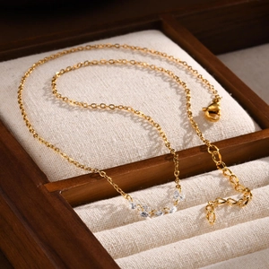 Detailed view of a gold-toned necklace with white zircons and lobster clasp on jewelry box